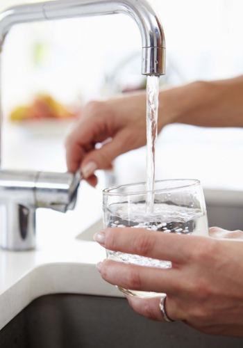 Mano de mujer sujeta un vaso mientras se llena de agua de un grifo